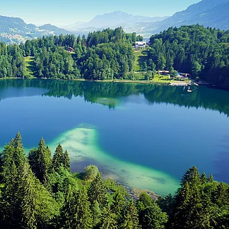 Blick von der Skiflugschanze in Oberstdorf auf den tiefblauen Freibergsee umgeben von grünem Wald