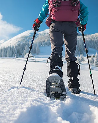 A woman with a backpack in snowshoes climbs a snowy mountain
